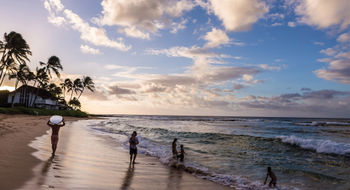 A surfer and a family enjoy the sunrise on a Kauai beach.