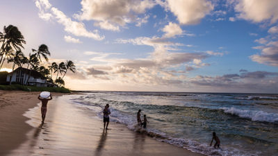 A surfer and a family enjoy the sunrise on a Kauai beach.