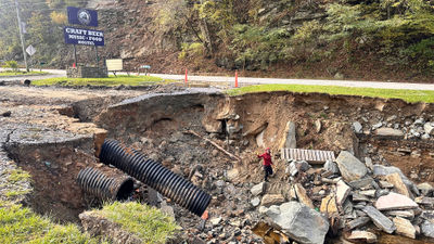 Cruise editor Andrea Zelinski waves from a pit created when Hurricane Helene destroyed part of the parking lot at The Station at 19E, an Appalachian Trail hostel in Roan Mountain, Tenn.