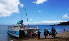 Guests line up and take turns boarding the catamaran, being careful to time it with the waves.