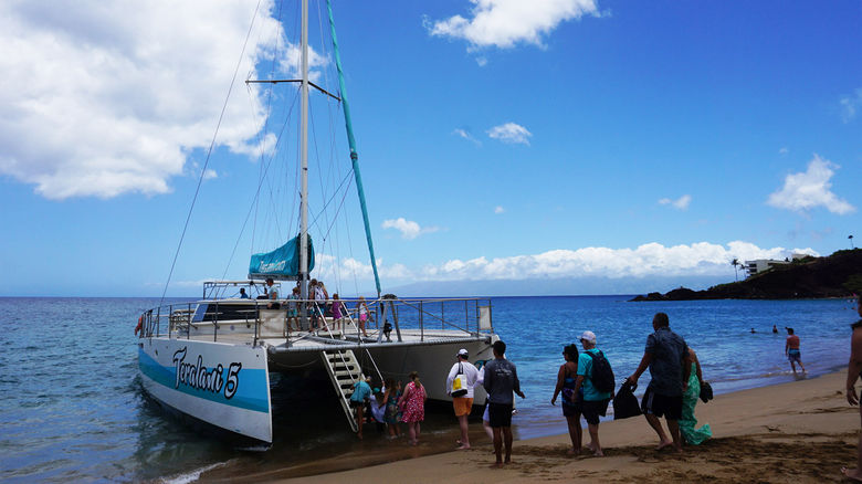 Guests line up and take turns boarding the catamaran, being careful to time it with the waves.